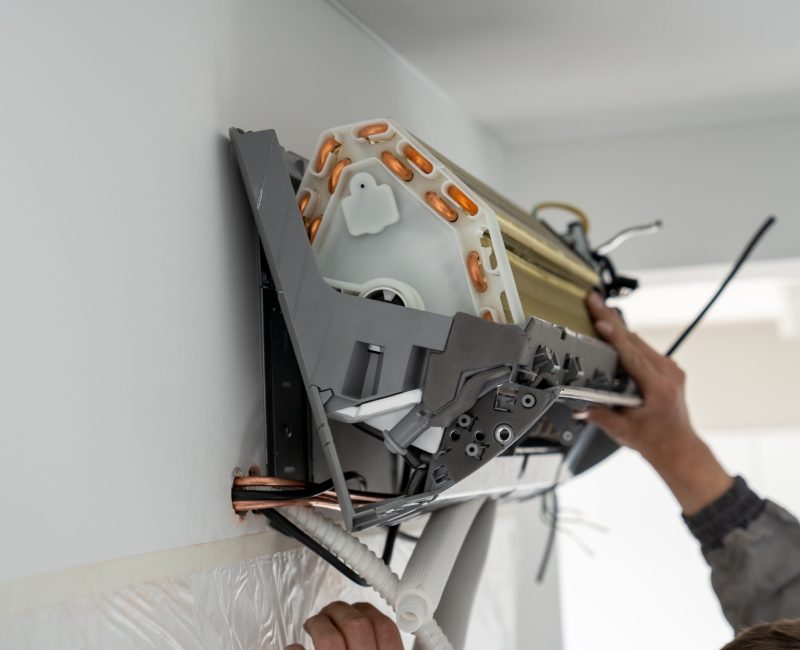 Hands of man technician in uniform installing air conditioner in apartment on wall. Maintenance and repair service concept. Creating pleasant microclimate for living. Climate control, split system.